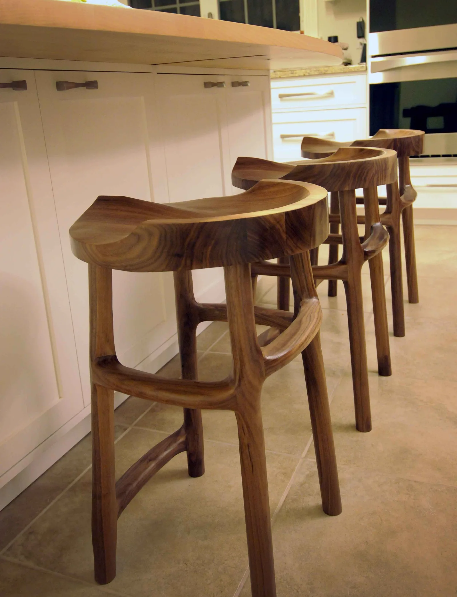 Carved walnut counter stools lined up at a kitchen island