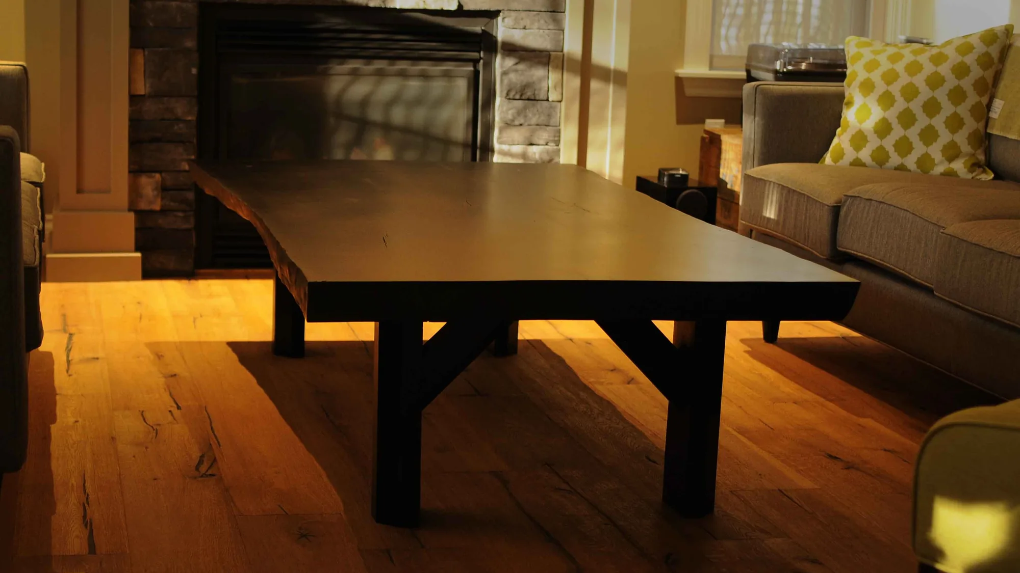 Low slab coffee table with a dark finish and trestle legs, lit by evening sun in a living room