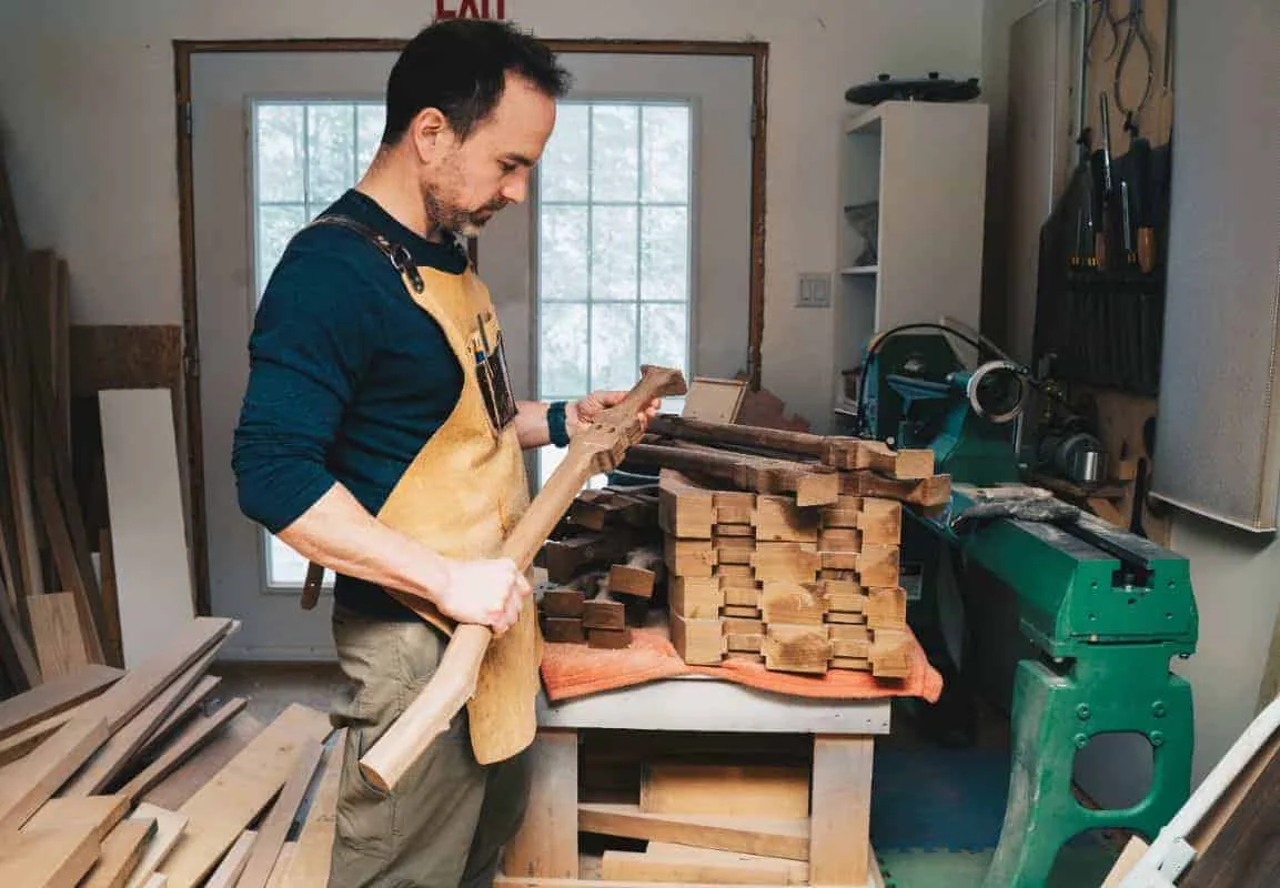 Michael McQuaid at his bench, shaping a carved chair part beside a stack of cut pieces