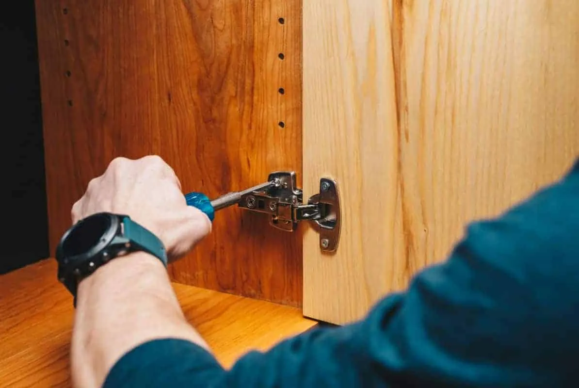 Close view of a hinge being adjusted inside a cherry cabinet